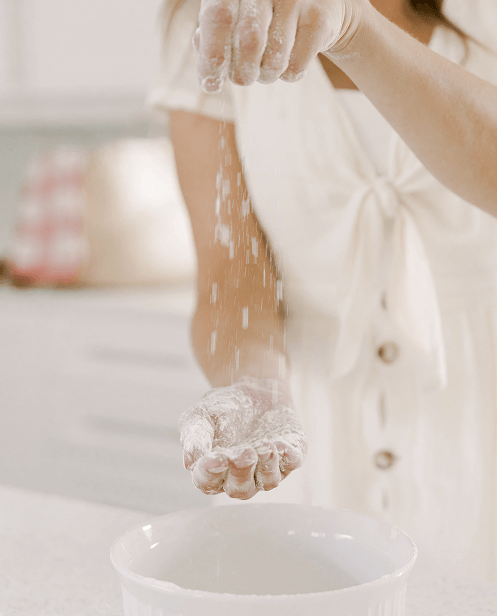 mom with flour on hands while baking in kitchen wearing a white dress